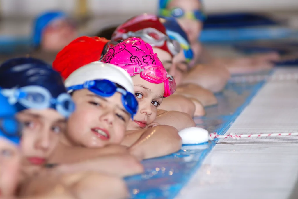 Crianças com toucas de natação participando de aula prática em piscina em Xapuri.
