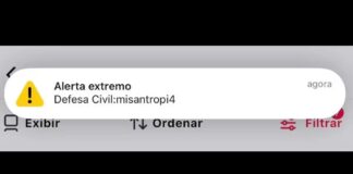 Celular exibindo alerta falso da Defesa Civil no Acre com elementos de segurança digital ao fundo